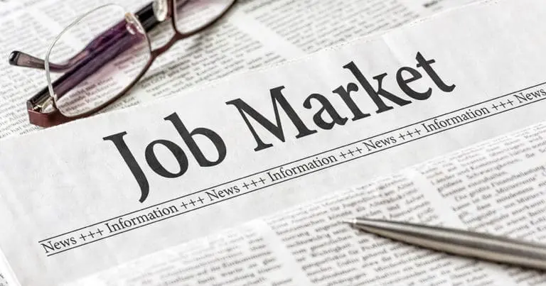 Newspaper with a headline that reads Job Market with a pair of glasses and a pen resting on it