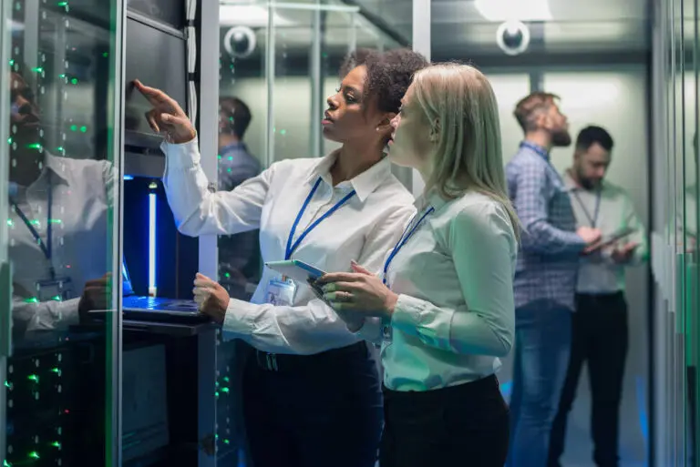 image of two women standing in a computer server room and looking at a screen together to symbolize IT project scope creep