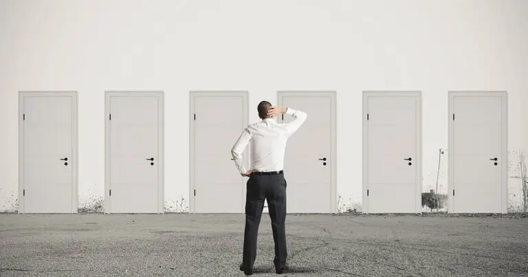 A man in business attire stands with his back to the viewer, scratching his head while facing a row of six identical closed white doors. The setting is minimalistic, with a plain wall and a gray concrete floor, symbolizing decision-making or choosing between multiple options.