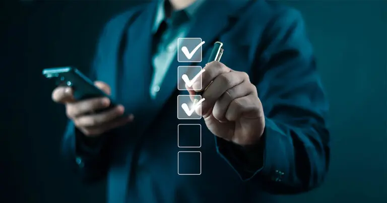 A person in a dark business suit is holding a smartphone in one hand and using a pen in the other hand to mark checkboxes on a virtual checklist. Three checkboxes are checked, and one remains empty to symbolize essentials for an effective job description. The background is blurred, emphasizing the professional setting.