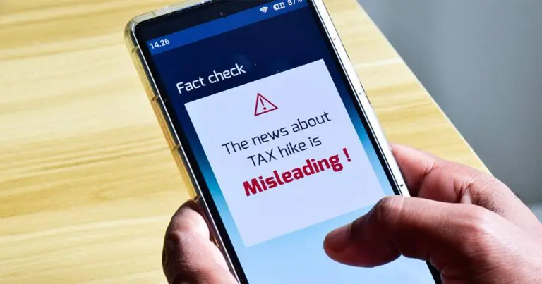 Image of hands holding a mobile phone. On the phone's screen a warning message reads 'the news about tax hike is misleading' to represent metas fact checking