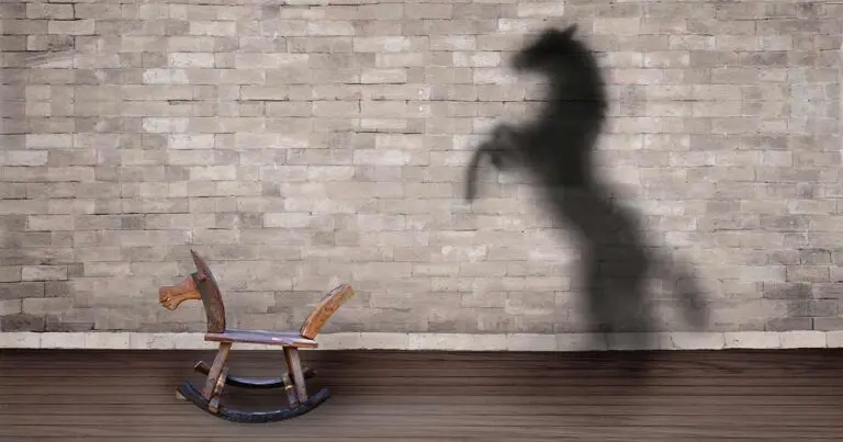 A small wooden rocking horse sits on a wooden floor against a brick wall, casting a large shadow of a powerful, rearing horse. The contrast between the simple toy and its bold shadow symbolizes hidden potential, untapped talent, or the idea of seeing beyond surface appearances to recognize greater abilities.