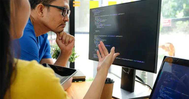 Two professionals at a desk looking at a computer screen with lines of code looking quizzical to represent AI model collapse