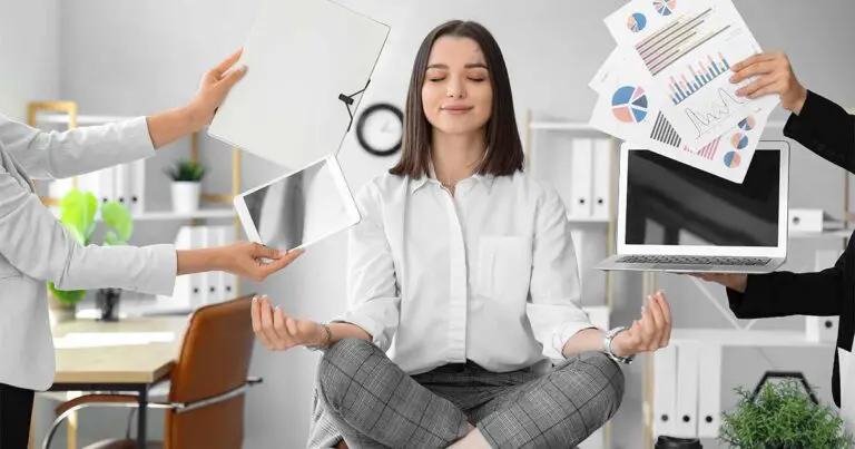 A woman sitting on a desk with her legs crossed in a meditation pose surrounded by off camera people trying to present her with various documents, computers, and electronics.