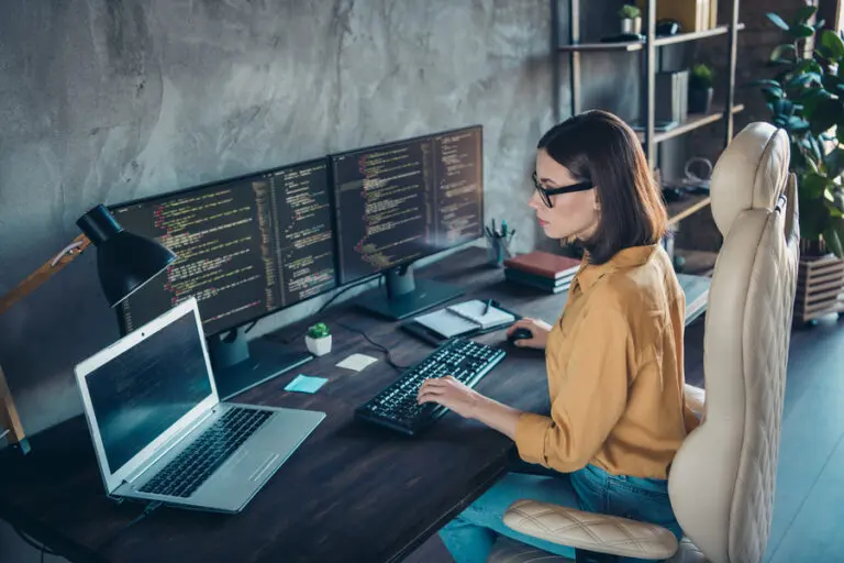 Profile side view portrait of focused skilled woman web developer using laptop at workplace workstation indoors