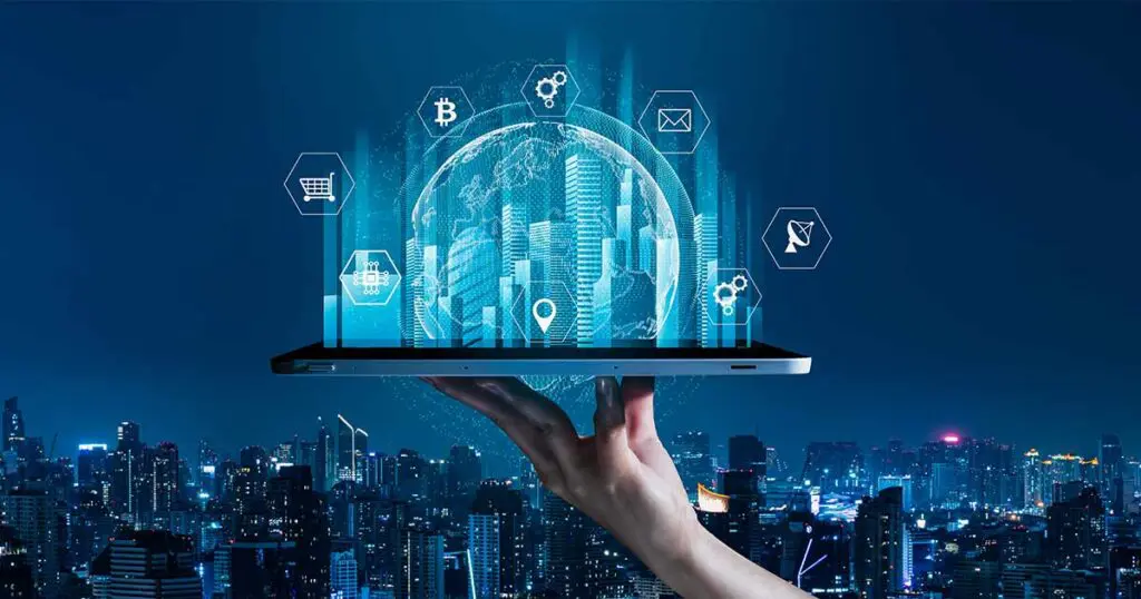 A person holds a digital tablet above a city skyline at night. Emerging from the tablet is a holographic-style digital globe surrounded by icons representing technology and digital tools, including cryptocurrency, email, cloud computing, location, and shopping cart symbols. The city lights below emphasize the contrast between physical and digital infrastructure.