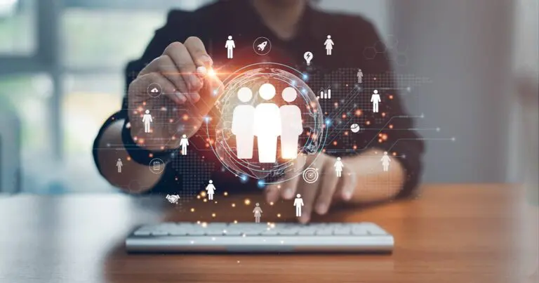 A person works at a desk, interacting with a glowing digital interface that displays interconnected icons of people and data points, suggesting technology-driven talent management. A central graphic of three figures appears within a bright sphere, surrounded by symbols for analytics, communication, and growth. The scene conveys a modern, tech-focused approach to mondo international staffing services/