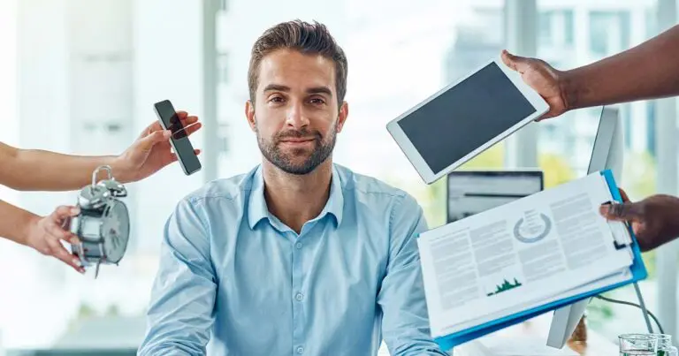 A man sits calmly at a desk while multiple hands around him hold a smartphone, tablet, alarm clock, and paperwork, all directed toward him at once. The scene conveys workplace pressure and constant digital and time-based demands competing for his attention.
