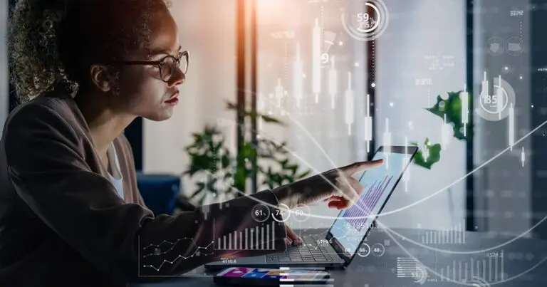 A professional sits at a desk using a laptop, pointing at the screen as translucent charts, graphs, and data indicators overlay the scene. The visual suggests close interaction with digital systems and analytics, conveying themes of trust, oversight, and decision-making in IT asset management.