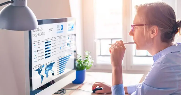 A woman sits in a bright sunny room at a desk looking at a computer with website analytics on the screen.