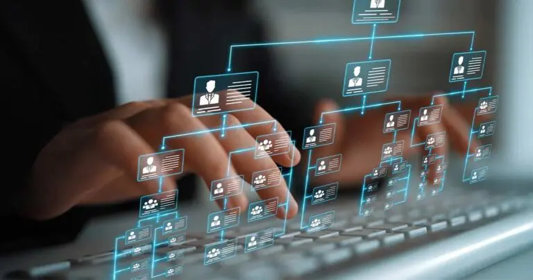 Hands type on a laptop keyboard while a glowing, digital organizational chart with employee icons and connecting lines hovers above the keys. The visual suggests workforce structure, planning, and human roles layered over modern technology, emphasizing people-focused strategy in a digital workplace.