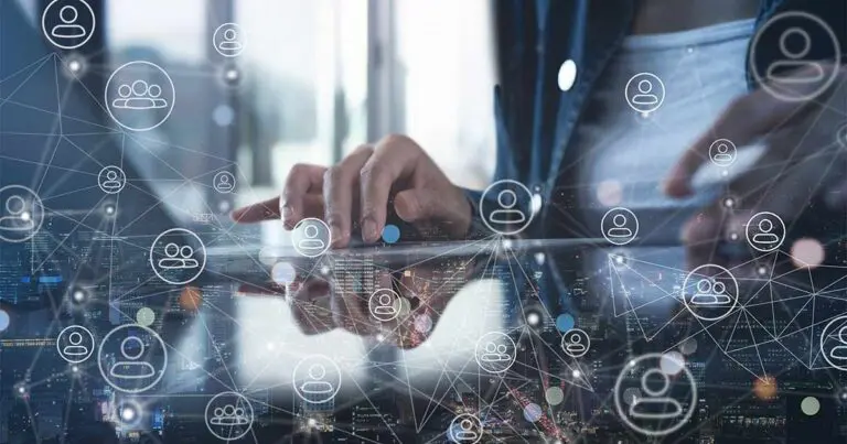 A person sits off camera with only their torso and hands visible typing on a laptop with a digital overlay of interconnected symbols of profile icons scatter the screen to symbolize the AI hiring process