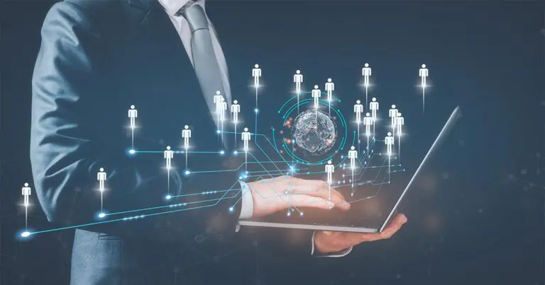 Business professional in a suit uses a laptop while glowing digital icons of people connect through circuit-like lines around a central globe. Futuristic network graphics suggest global communication, data sharing, or remote workforce technology.
