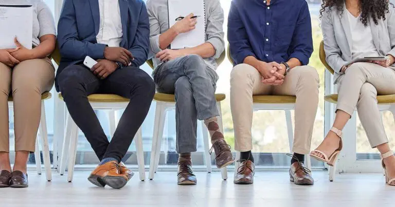 A photo of several professional individuals sitting in a row on chairs with their heads out of frame to symbolize hiring quality and anonymity in the job market