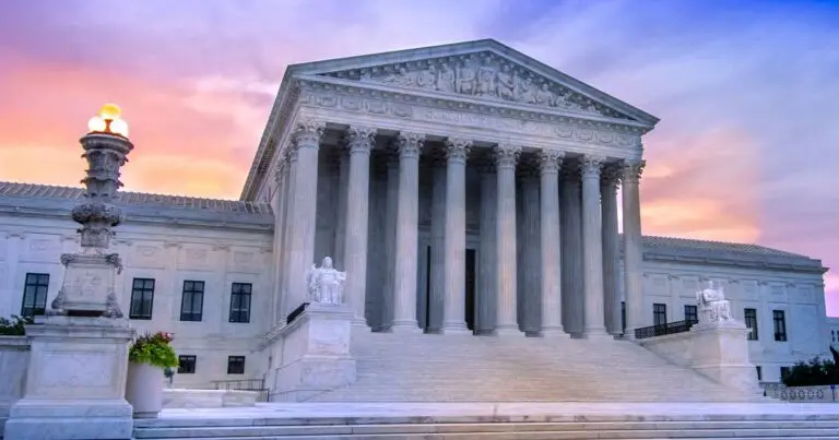 Image of the supreme court building. a white building with columns and a peaked roof atop a large staircase at sunset with a purple and pink sky