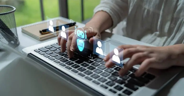 Hands typing on a laptop keyboard with glowing digital icons of user profiles and a chatbot floating above the keys, illustrating AI-assisted hiring or workforce automation. A blurred office setting and notebook in the background create a modern, tech-focused atmosphere.