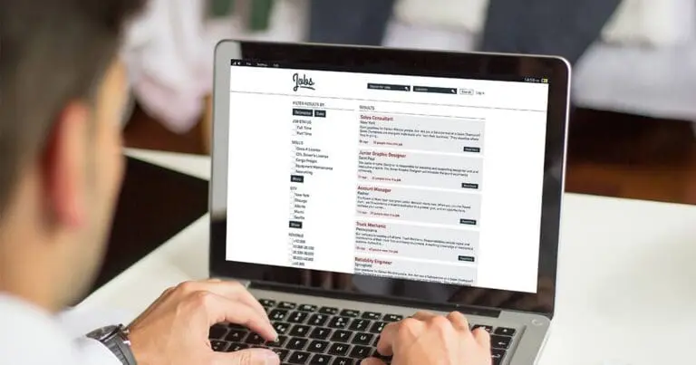 Person typing on a laptop while browsing an online job board showing multiple job listings and search filters. The screen displays openings for roles such as sales consultant, graphic designer, and account manager, illustrating the challenge of spotting fake or “ghost” job postings during an online job search.