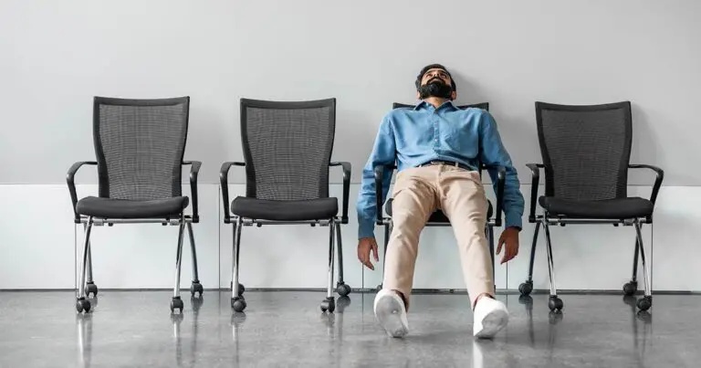 A job candidate slumps low in a chair in a waiting area, head tilted back and arms hanging at their sides, with several empty chairs beside them. The scene conveys boredom, fatigue, or disengagement, reinforcing the idea of unproductive or uninspired interview questions and suggesting a need for more thoughtful conversation.