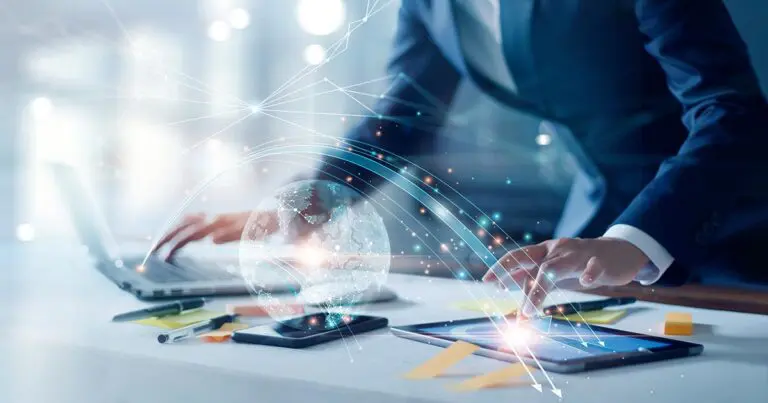 A business professional works across a laptop and tablet as a glowing digital globe and interconnected data pathways overlay the workspace, symbolizing global connectivity and technology-driven operations. The futuristic visual supports the theme of digital transformation, highlighting the flow of information, collaboration, and the human role in implementing change.