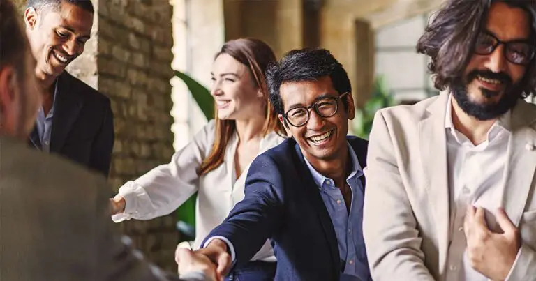 Four professionals smile and laugh together during an in-person conversation, illustrating the value of networking and personal connection in the age of AI and remote work.