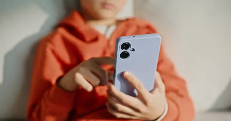 A child in an orange hoodie holds and taps a smartphone, illustrating young people’s engagement with social media amid growing scrutiny of tech governance.