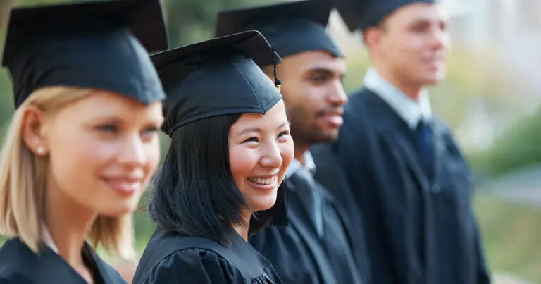 Four smiling graduates in black caps and gowns stand together outdoors, reflecting the transition from higher education to the workforce.