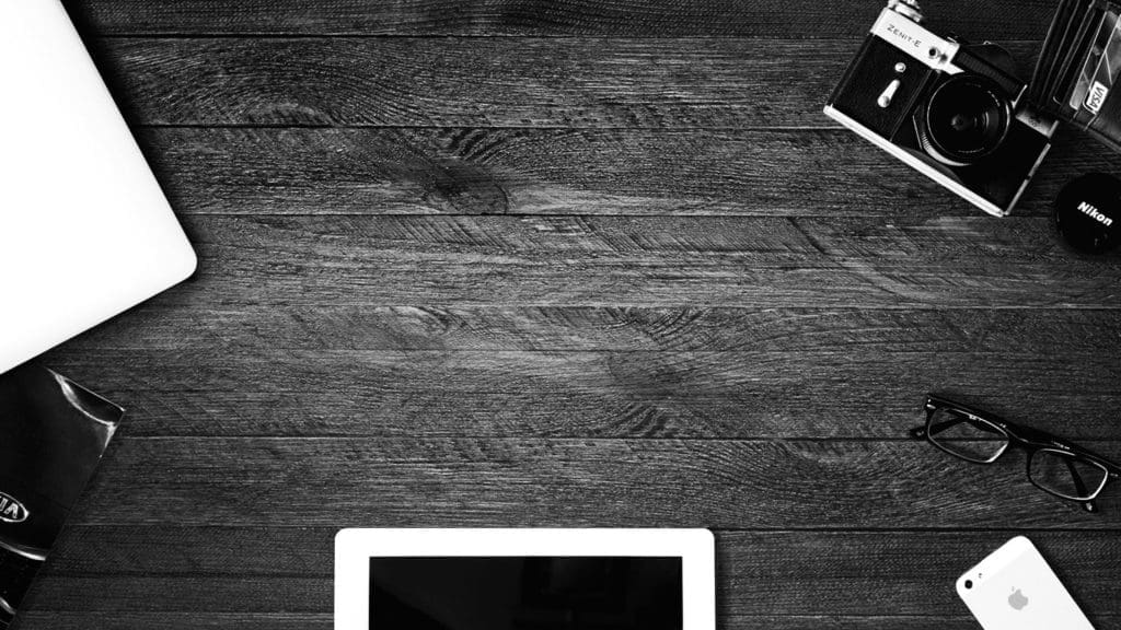 black and white photo of items on a wooden desk, ipad old camera glasses etc