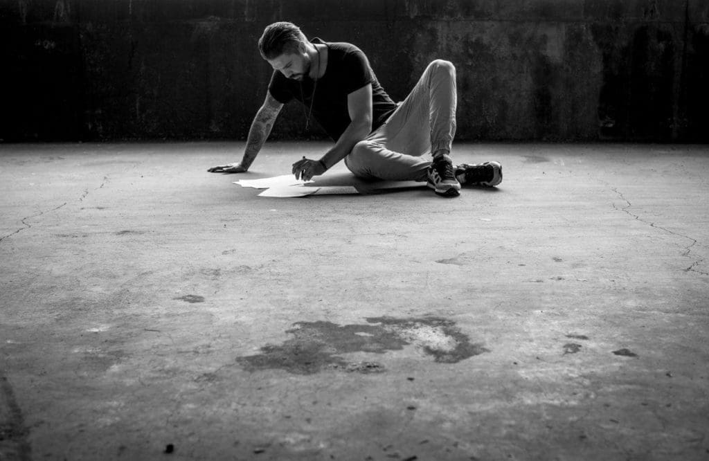 young person on a concrete floor of an empty building drawing on paper