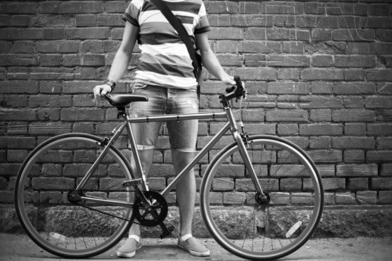 person holding a bicycle outdoor next to a brick wall