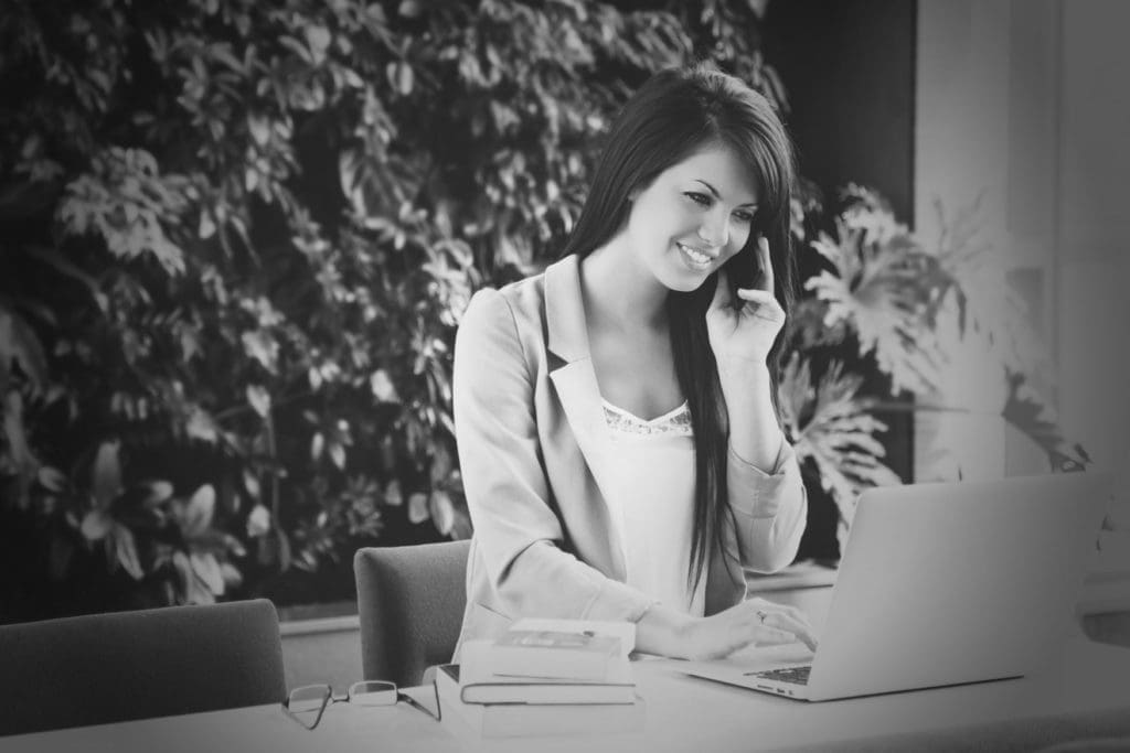 a smiling woman on a phone while working on a laptop in an office