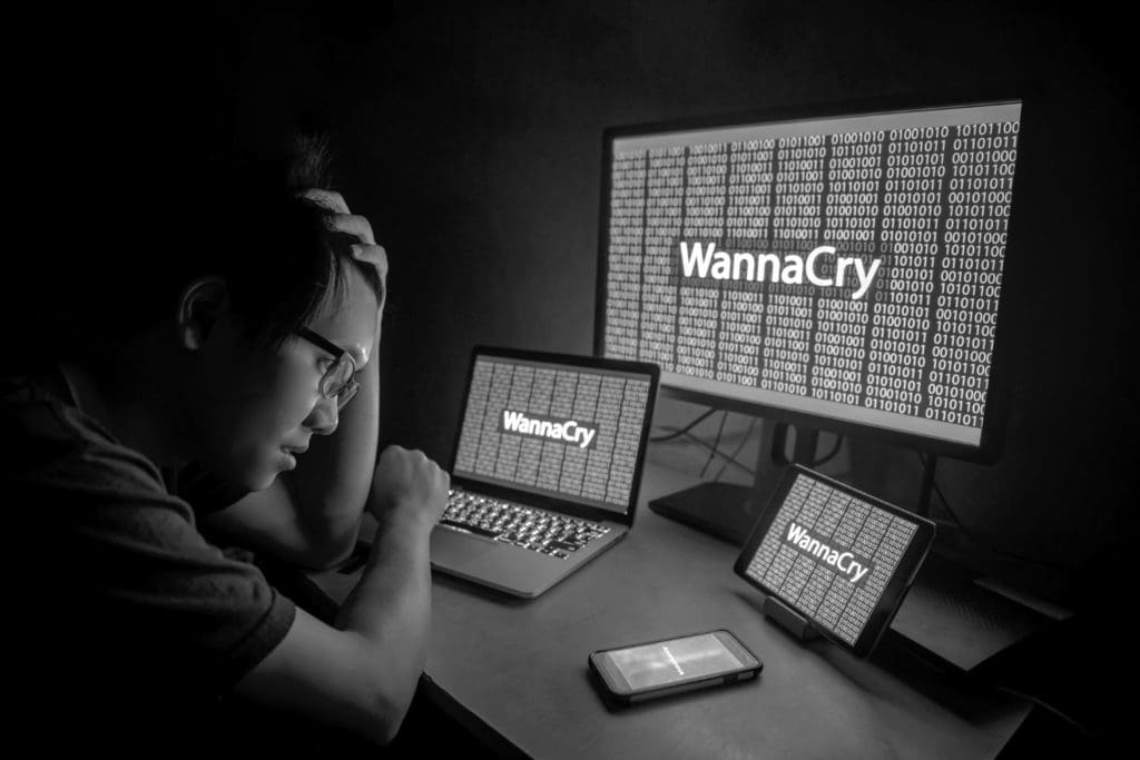 visibly frustrated person in front of several monitors which display wannacry on their screens