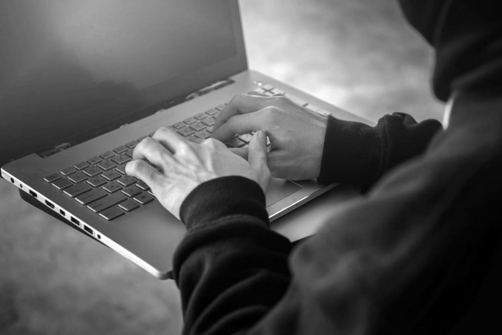 A programmer wearing a hoody faces a computer monitor while writing code