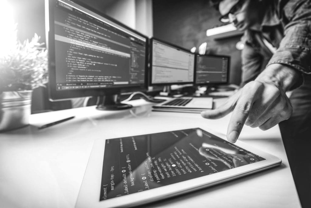 Several monitors and a tablet all displaying code on a desk of a computer professional