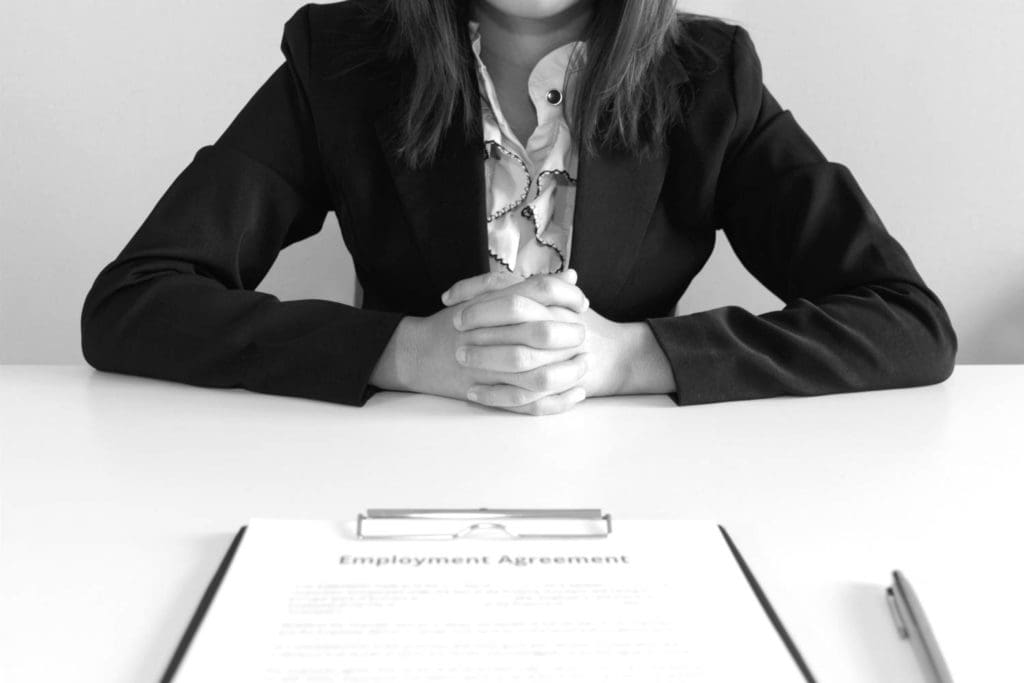 Woman dressed in a business suite sitting at an interview across from employment agreement paper
