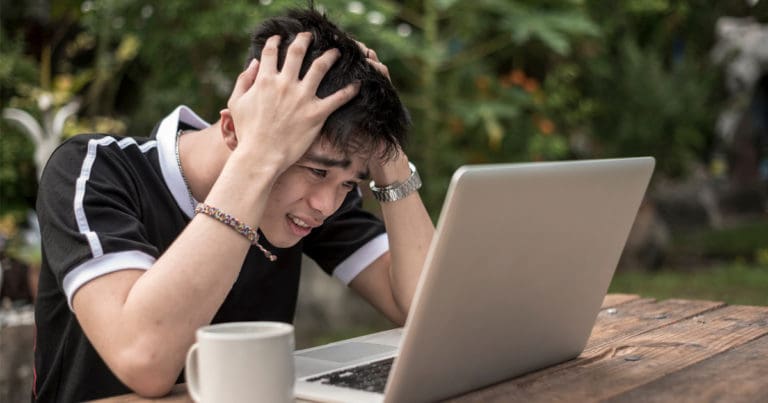 Frustrated man with hands on his head looking at a laptop