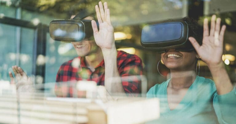 photograph taken through a reflective window of two people wearing virtual reality headsets and smiling
